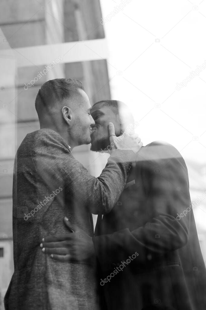Black and white reflection in glass of two kissing men, afro american and caucasian.