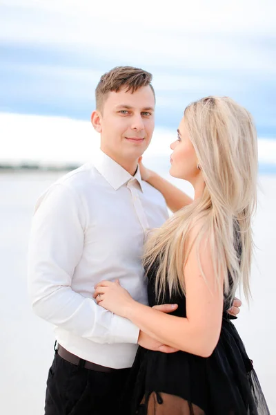 Young handsome husband in white shirt hugging wife wearing black dress in winter steppe. — Stock Photo, Image