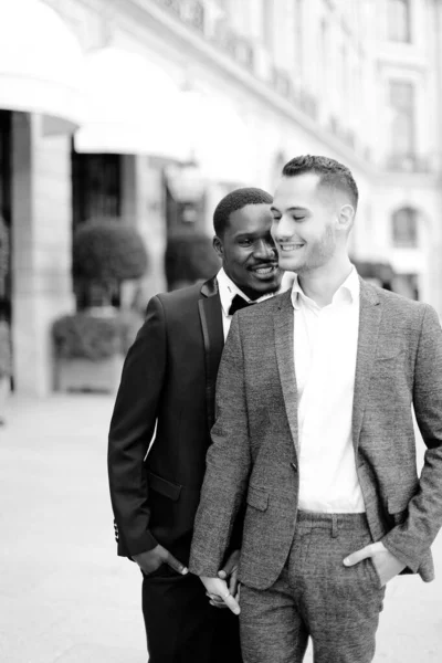 Zwart en wit foto van afro amerikaanse knappe man knuffelen europees jongen dragen pak. — Stockfoto