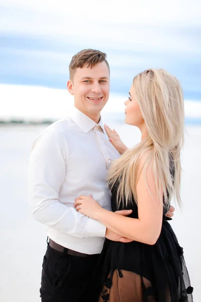 Young smiling husband in white shirt hugging wife wearing black dress in winter steppe. — Stock Photo, Image