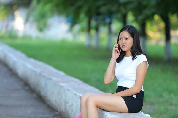 Mladá dívka sedí a mluví po telefonu v parku — Stock fotografie