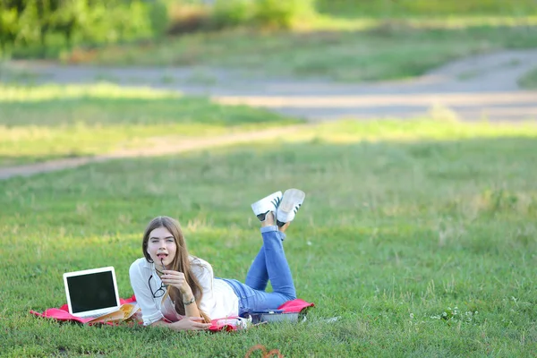 Jeune fille couchée sur l'herbe dans le parc et travaille à un ordinateur portable . — Photo