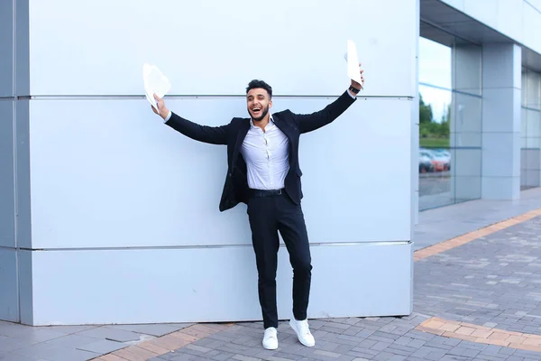 Hombre joven árabe hombre de negocios riendo, regocija el éxito, sostiene papeles y puestos en el fondo del centro de negocios . — Foto de Stock