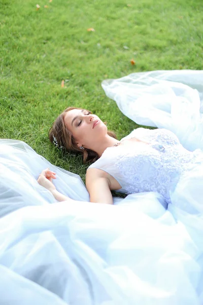 Αθώα όμορφη νύφη ξαπλωμένη στο γρασίδι σε κιβωτό και φορώντας λευκό φόρεμα. — Φωτογραφία Αρχείου