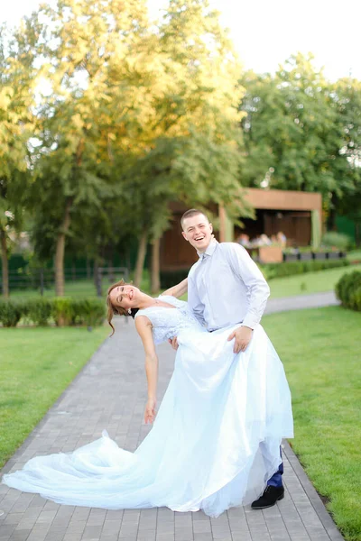 Young european bride dancing with groom in park and wearing white dress. — Stock Photo, Image