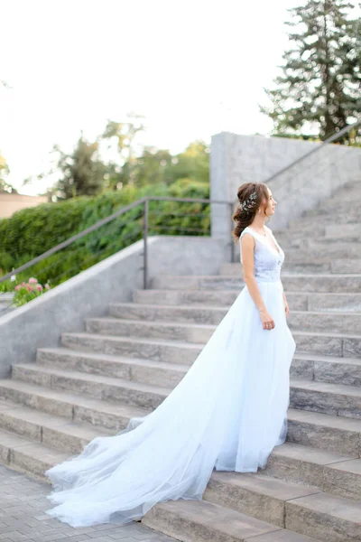 Πίσω όψη της ευρωπαϊκής νύφης με τα πόδια σε τσιμεντένιες σκάλες και φορώντας λευκό φόρεμα. — Φωτογραφία Αρχείου