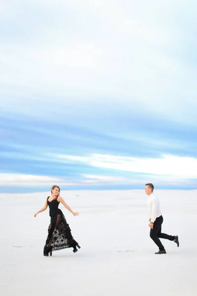 Молода жінка і чоловік бігають в зимовому степу, одягнені в чорне плаття . — стокове фото