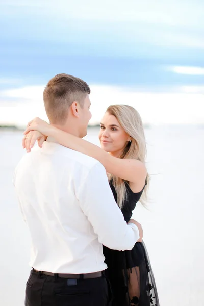 Young girl wearing black dress hugging man in winter field background. — Stock Photo, Image