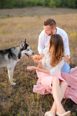 Genç Amerikalı kız ve oğlan çimenlerde oturuyor ve Husky 'i besliyor..