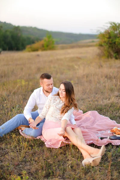 Νεαρή γυναίκα και άντρας κάθονται πάνω σε ροζ καρό στη φύση. — Φωτογραφία Αρχείου