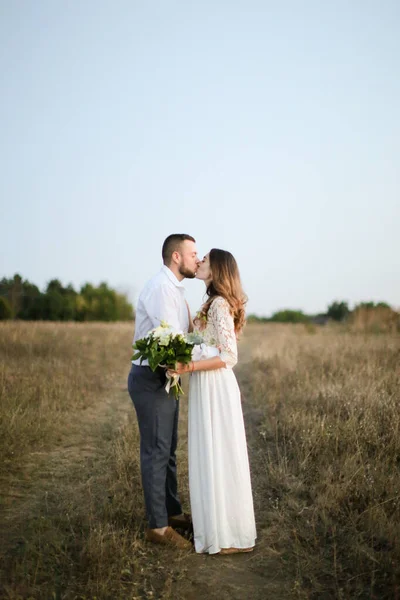 Γαμπρός φιλιά νύφη με μπουκέτο λουλούδια στο φόντο στέπα. — Φωτογραφία Αρχείου