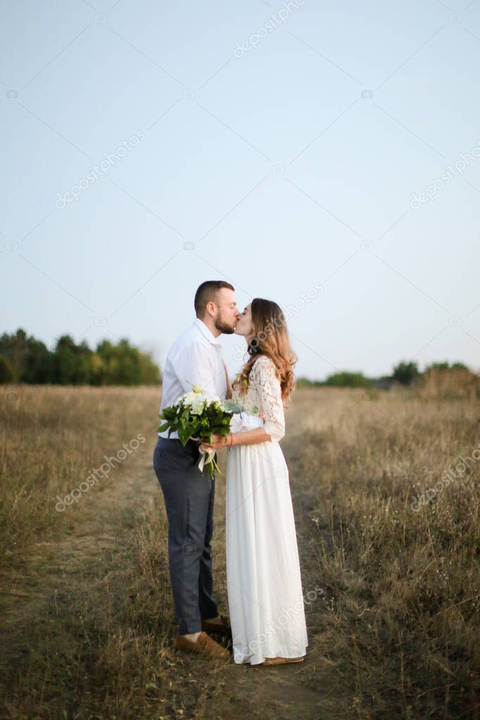 Groom kissing bride with bouquet of flowers in steppe background.