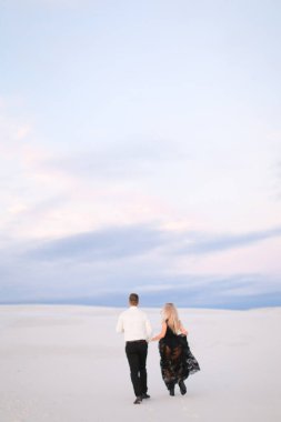 Siyah elbiseli genç bir adam ve beyaz bir kadın kar bozkırında yürüyor..