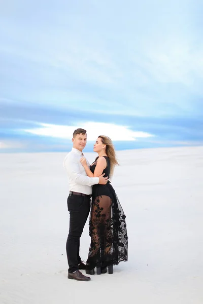 Jovem marido de camisa branca abraçando esposa vestindo vestido preto na estepe de inverno . — Fotografia de Stock