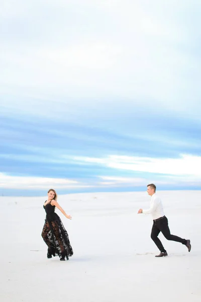 Молода дівчина і чоловік бігають в зимовому степу, одягнені в чорну сукню . — стокове фото