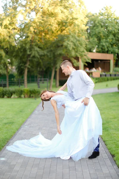 Young charming bride dancing with groom in park and wearing white dress. — Stock Photo, Image