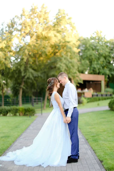 Giovane sposa tenera in piedi con sposo caucasico e tenendosi per mano in giardino . — Foto Stock