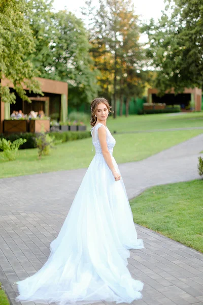Λευκή νύφη στέκεται στον κήπο και φοράει μακρύ λευκό φόρεμα. — Φωτογραφία Αρχείου