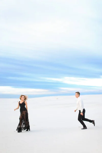 年轻的女士和男人穿着黑色的连衣裙在冬季的草原上奔跑. — 图库照片
