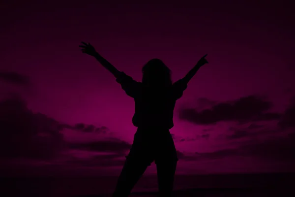 Female silhouette with raised hands on violet sunset sky background in Thailand.