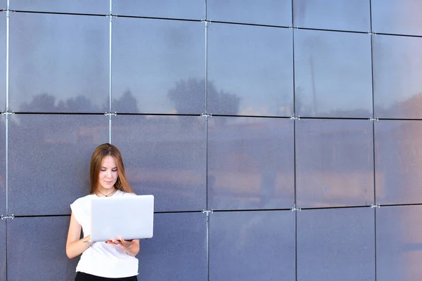 Mooi jong meisje ondernemer houdt laptop en werkt, lost problemen op, en staat op de achtergrond muur van business center. — Stockfoto