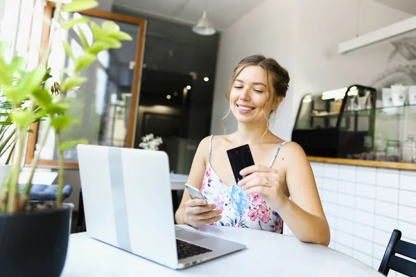 Young woman holding smartphone and credit card near laptop.