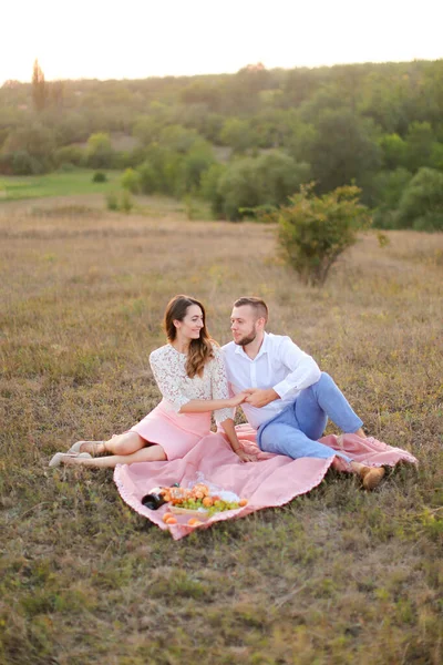 Feliz casal romântico sentado em xadrez rosa com garrafa e frutas no campo . — Fotografia de Stock