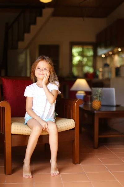 Niña feliz sentada en silla de madera en la sala de estar . — Foto de Stock