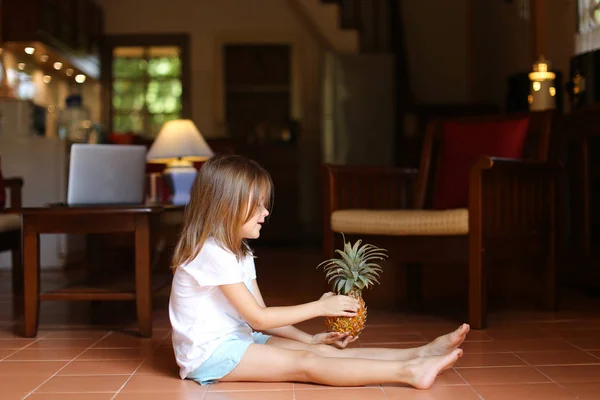 女の子は床に座ってパイナップルと遊ぶ. — ストック写真