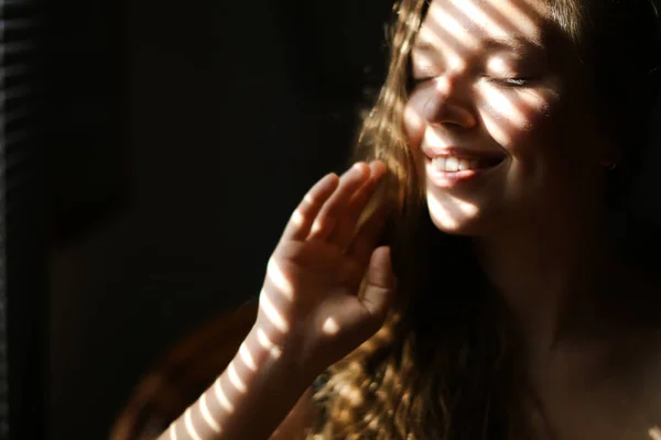 Close up portrait of young smiling woman with closed eyes and striped shadows.