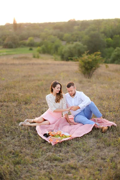 Happy caucasian couple sitting on pink plaid in field. — Stockfoto