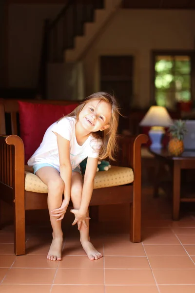 Niña sonriente sentada con juguete en silla de madera . — Foto de Stock