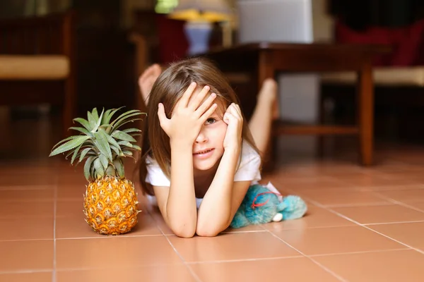 Retrato de una niña linda tumbada en el suelo con piña y juguete . — Foto de Stock