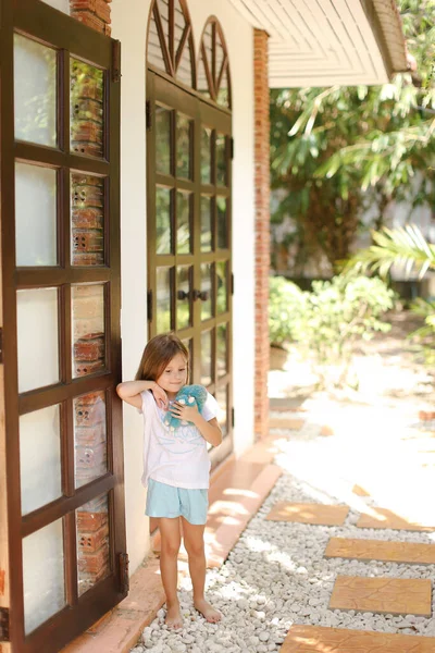 Poco descalza chica de pie cerca de la puerta de madera con juguete exterior . — Foto de Stock