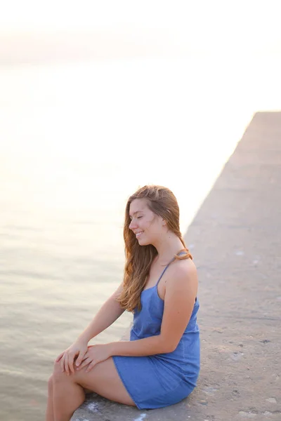 Jovem mulher sentada no cais e vestindo sundress — Fotografia de Stock