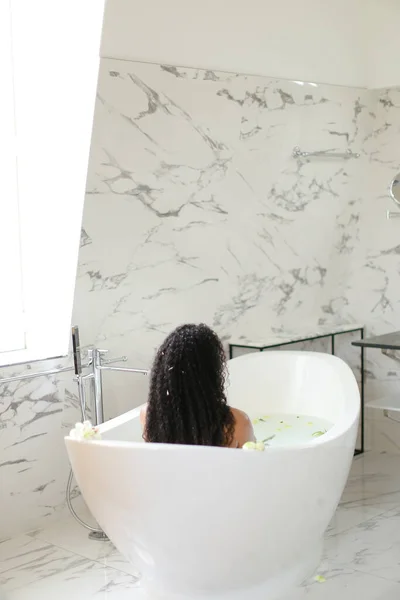 Back view black girl taking milk bath with flowers. — Stock Photo, Image