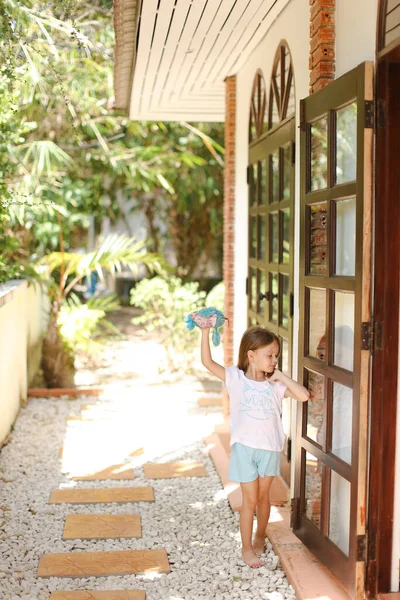 Pequeña chica descalza parada cerca de la puerta y jugando con el juguete afuera . — Foto de Stock