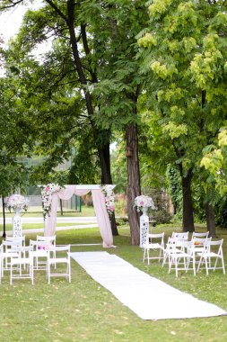 Muhteşem bir düğün kemeri, parkta güller ve sandalyelerle süslenmiş..
