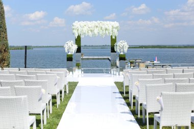 Beyaz harika düğün kemeri ve göl kenarındaki sandalyeler.