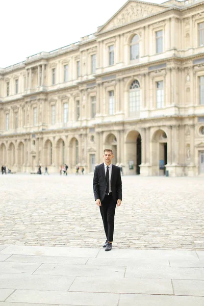 Junger Mann im schwarzen Anzug spaziert durch Paris, Gebäude im Hintergrund. — Stockfoto