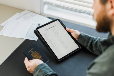 Vize başvurusunu tablet ve içi boş pasaportla okuyan bir erkek.