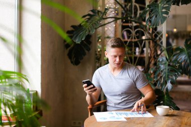 Kafede belgeler ve cep telefonuyla çalışan Avrupalı işadamı.