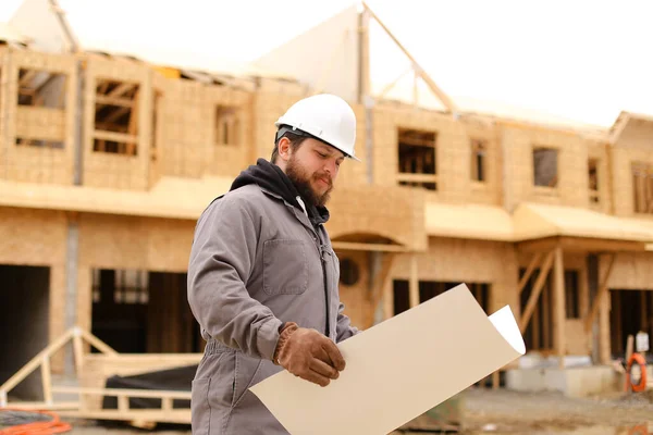 Foreman segurando plano de desenho de arquitetura em papel no canteiro de obras . — Fotografia de Stock