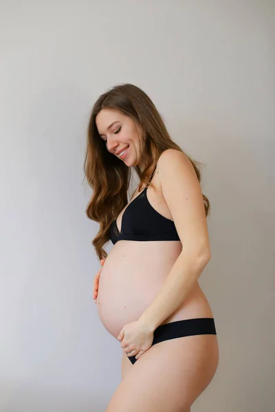 Mulher grávida em lingerie preta segurando sua barriga em fundo espaço cópia cinza . — Fotografia de Stock