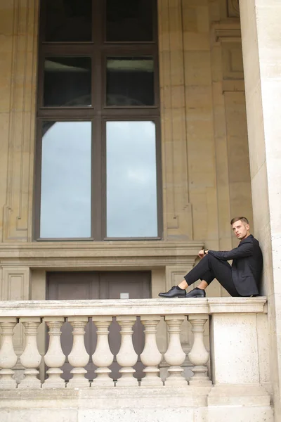Joven chico guapo sentado en el balcón barandilla de hormigón en París . — Foto de Stock