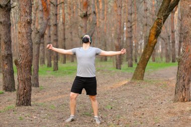 Elleri havada mutlu bir adam maske takıyor ve ormanda yürüyor..