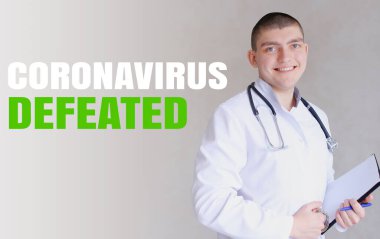 Kafkasyalı genç doktor yenilgiye uğramış Coronavirüs yüzünden seviniyor ve gri duvar arka planında duruyor..