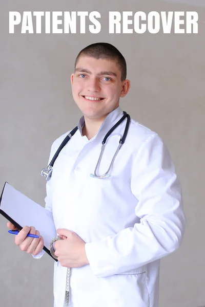 Mladý lékař raduje, protože pacienti zotavují a stojí v šedé zdi pozadí. — Stock fotografie