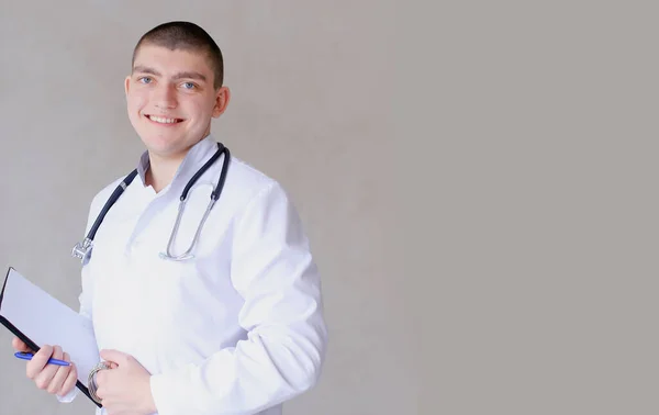 Giovane medico isolato in piedi con carte e stetoscopio in bachground grigio con spazio per la copia . — Foto Stock