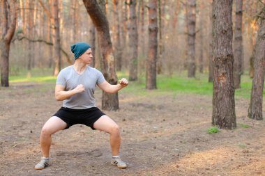 Genç adam spor yapıyor ve sabah parkında çömeliyor..